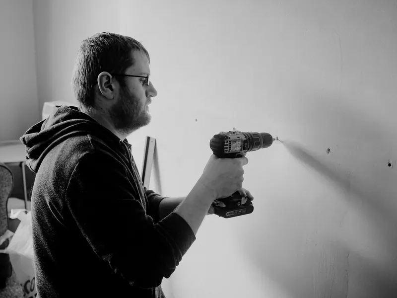 Man using a power drill to repair a wall inside a home. Black and white photo