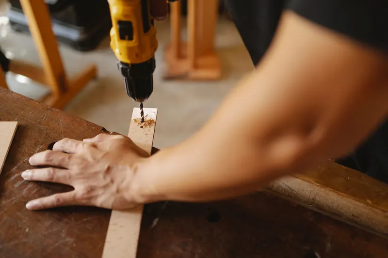 Crop anonymous male fixing wooden plank and drilling hole while working on table in workshop