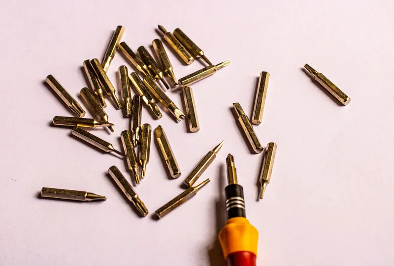 Close-up of various golden screwdriver bits with a handle on a white surface