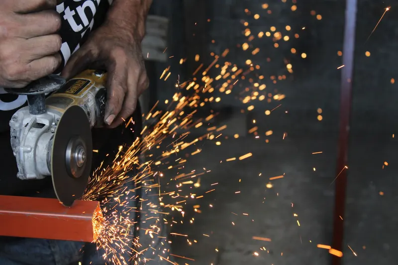A worker using a power tool creates sparks while cutting metal, showcasing industrial craftsmanship