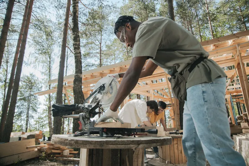Workers on a construction site cutting wood planks with a circular saw outdoors