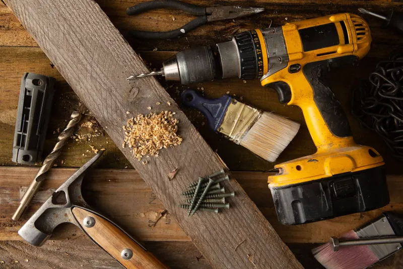 A close-up of various tools including a drill, hammer, and paintbrush on a wooden workbench